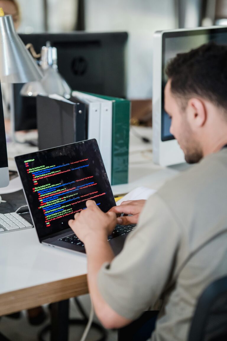 Focused software developer typing code on a laptop in a modern office setting.